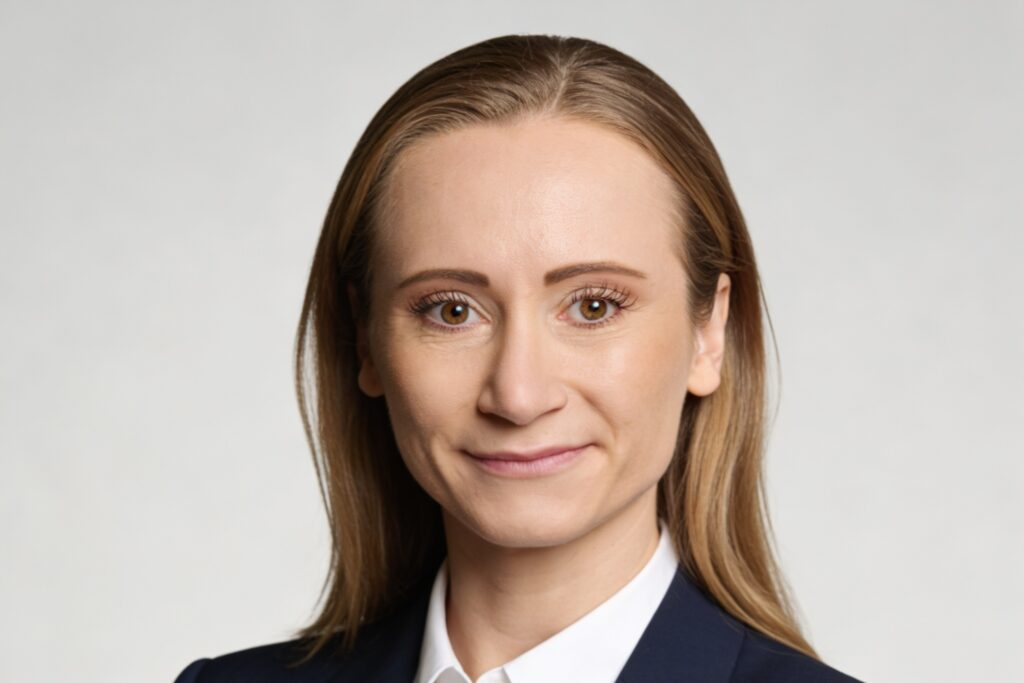 Close-up of a woman with light brown hair wearing a navy blazer and white shirt, looking at the camera.